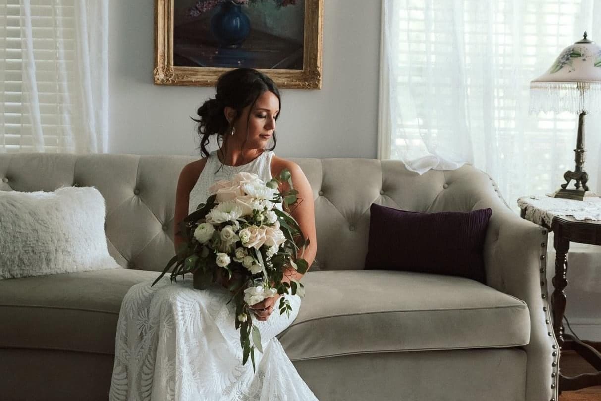 Bride sitting on a couch holding bouquet of flowers