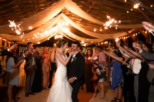 Bride and groom embrace while their guests hold sparklers around them at All 4 One Farms