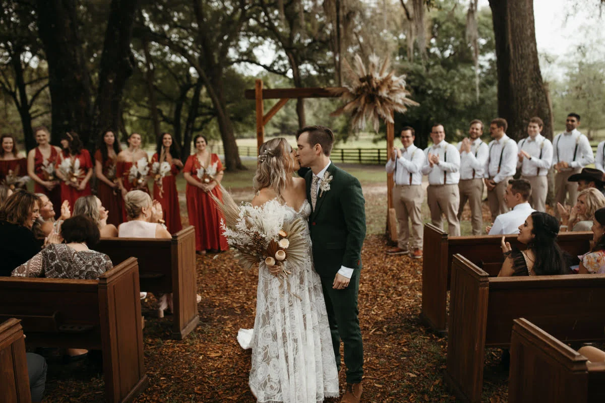 Bride and groom kissing after the ceremony while the guests and wedding party look on at All 4 One Farms