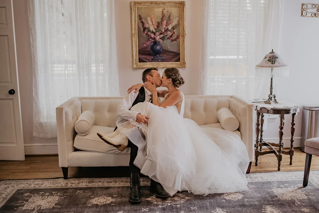 Bride and groom kissing in bride's room showing off the bride's cowboy boots at All 4 One Farms