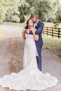 Groom embracing his bride on a roadway lines with a board fence at All4One Farms wedding venue.