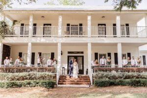 Bride and groom flanked by their wedding party on the two-story front porch of the manor house at All4One Farms wedding venue.