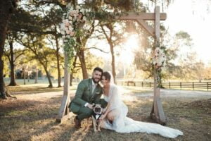 Bride and Groom kneel down next to their dog at sunset at All4One Farms wedding venue.