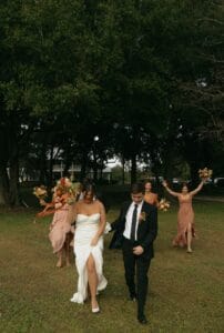 Bride and Groom lead their wedding party across the front lawn at All4One Farms. Ladies are holding their bouquets in the air.