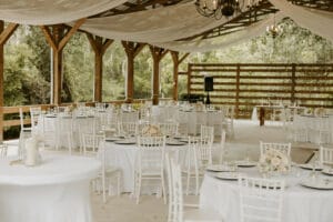 Reception set up with white linens, white china, white and light peach floral centerpieces, and white chairs.