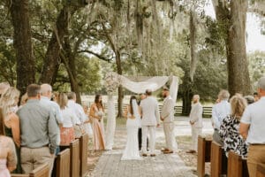 Bride's father with the bride at the alter with the groom and officiant under the shade of giant oak trees.