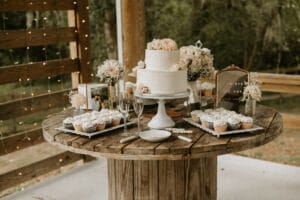 Dessert table with wedding cake in the center on a rustic spool table at All4One Farms.