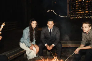 Couple sitting on wooden benches around a firepit roasting marshmallows at All4One Farms.