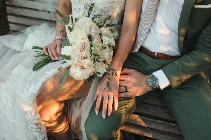 Bride and groom seated under the shade of oak trees with their hands resting on each others.