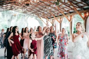 Bride tosses her bouquet and it hangs in the air as the single ladies reach their hands to catch it.