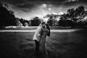 Bride and groom embrace in the field at All4One Farm with a dramatic skyline behind them.