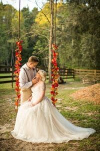 Bride seated on a swing and her groom looking into her eyes.